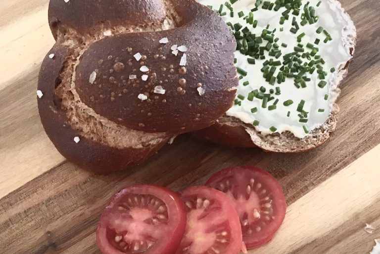 Ein Brötchen mit Frischkäse und Schnittlauch, serviert mit Tomatenscheiben.