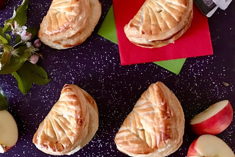 Gebackene Apfeltaschen auf einem dunklen Untergrund mit frischen Äpfeln.